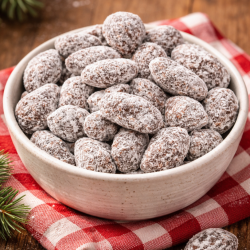 Mandorle al cioccolato fondente ricoperte di zucchero a velo e cannella in una ciotola su tavolo di legno