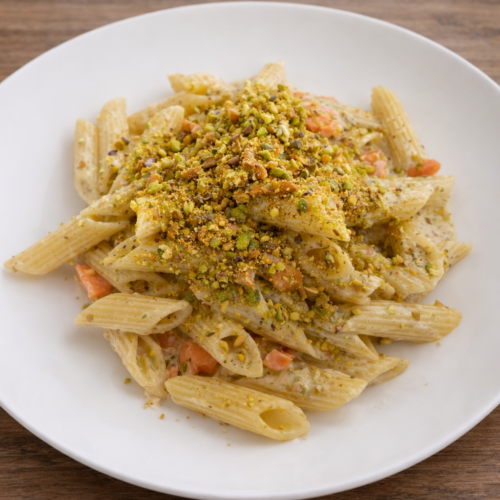 Pasta al mascarpone con pistacchi, salmone affumicato e scorza di limone servita su piatto bianco