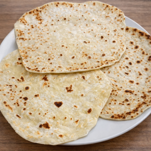 Piadine fatte in casa cotte in padella, disposte su piatto bianco su tavolo in legno