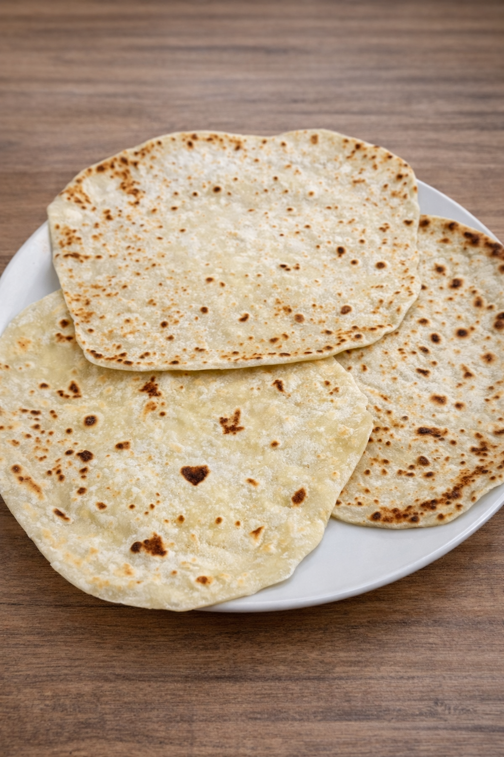 Piadine fatte in casa cotte in padella, disposte su piatto bianco su tavolo in legno