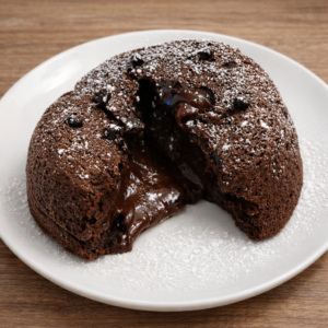 Tortino al cioccolato con cuore morbido e colata di cioccolato fuso, spolverato con zucchero a velo, servito su piatto bianco