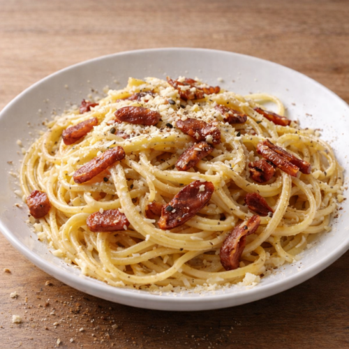 Pasta alla carbonara cremosa con guanciale croccante su piatto bianco